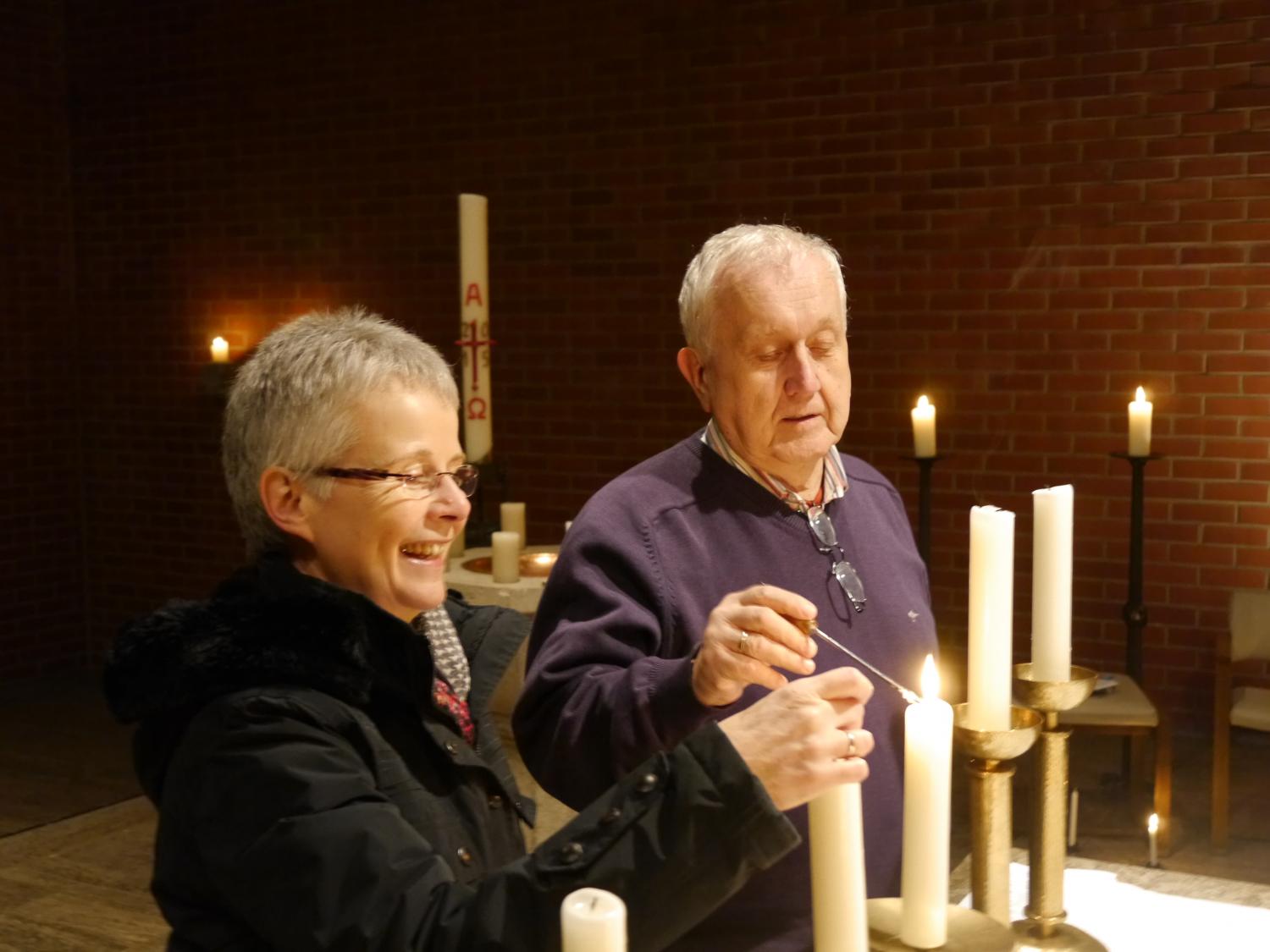 Eine Küsterin und ein Küster zünden gemeinsam Kerzen in einer Kirche an. (c) Bild: vocali einsfünf - In: Pfarrbriefservice.de Eine Küsterin und ein Küster zünden gemeinsam Kerzen in einer Kirche an.