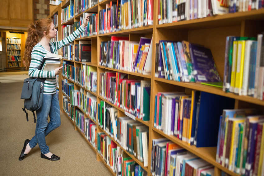 Redhead student taking book from shelf in the library at the university